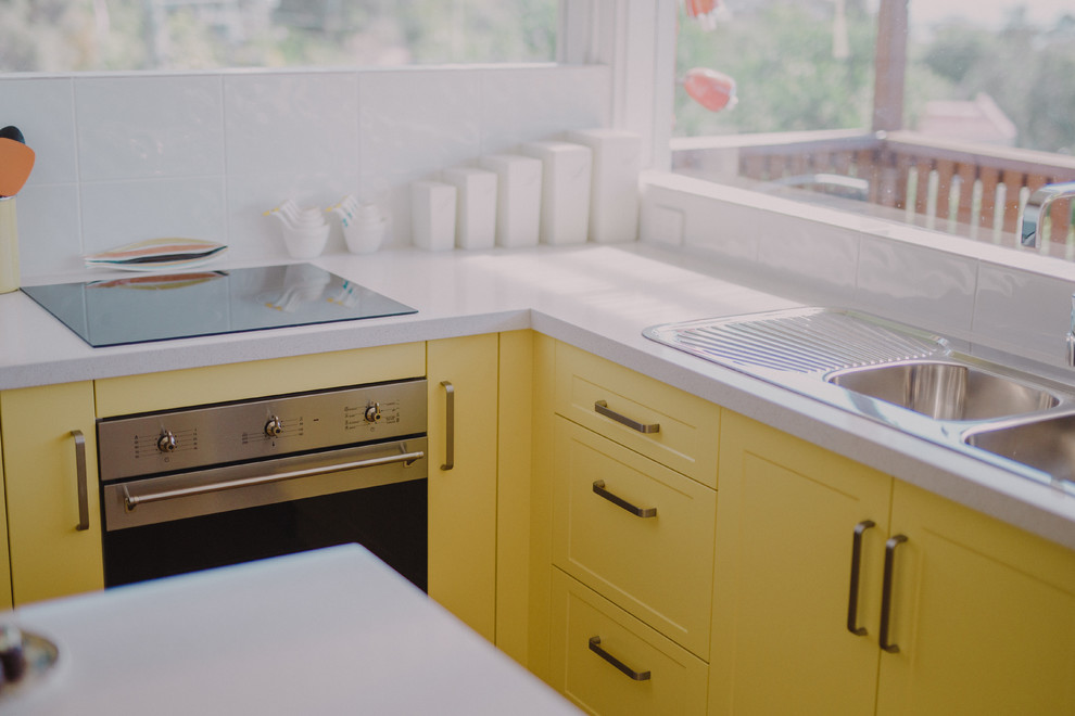 This is an example of a tropical kitchen in Hobart with yellow cabinets and with island.