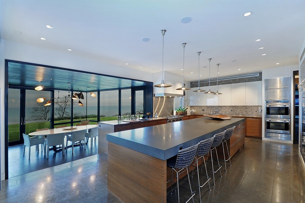 This is an example of a contemporary eat-in kitchen in Chicago with flat-panel cabinets, white cabinets, grey splashback and stainless steel appliances.