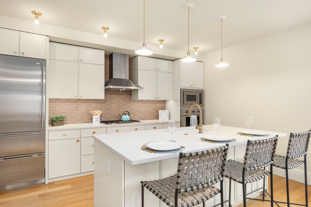 This is an example of a medium sized classic galley kitchen in Seattle with beige cabinets, engineered stone countertops, beige splashback, cement tile splashback, stainless steel appliances, an island and white worktops.