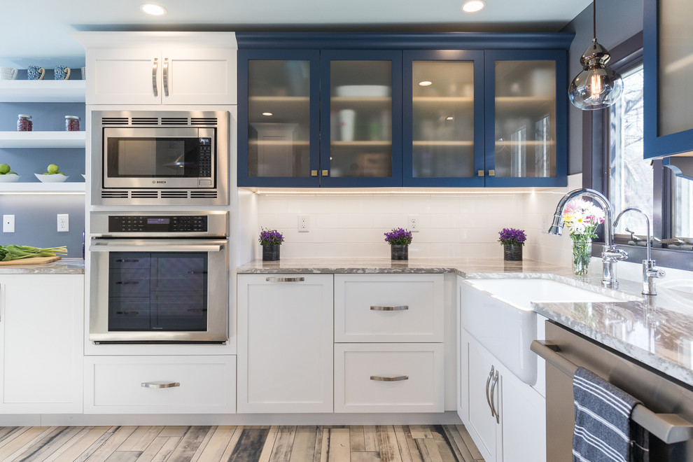 Photo of a mid-sized beach style l-shaped open plan kitchen in Manchester with a farmhouse sink, shaker cabinets, blue cabinets, glass benchtops, yellow splashback, ceramic splashback, painted wood floors and multi-coloured floor.