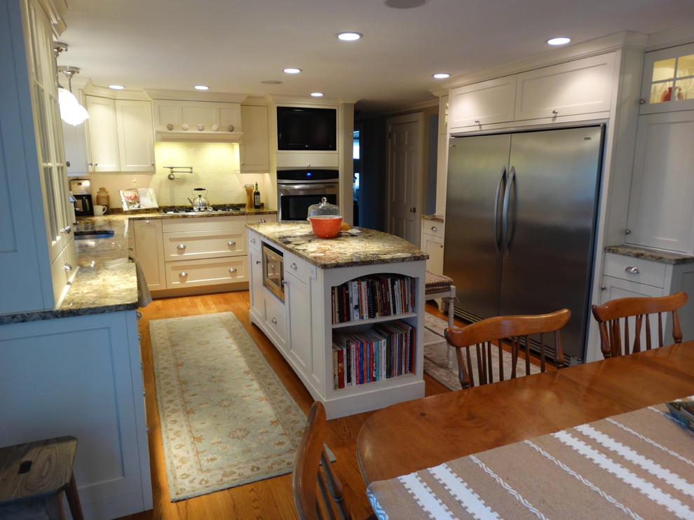 This is an example of a mid-sized country u-shaped eat-in kitchen in Boston with an undermount sink, shaker cabinets, white cabinets, granite benchtops, stainless steel appliances, light hardwood floors and with island.