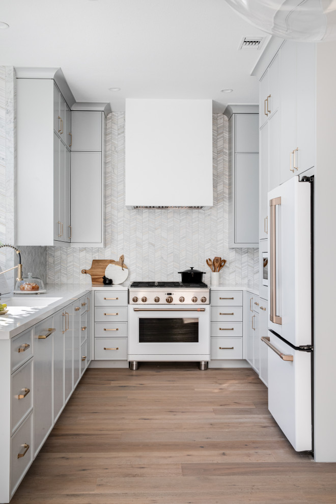 Idéer för att renovera ett avskilt, litet funkis vit vitt u-kök, med en undermonterad diskho, skåp i shakerstil, grå skåp, bänkskiva i kvarts, vitt stänkskydd, stänkskydd i marmor, vita vitvaror, mellanmörkt trägolv och brunt golv