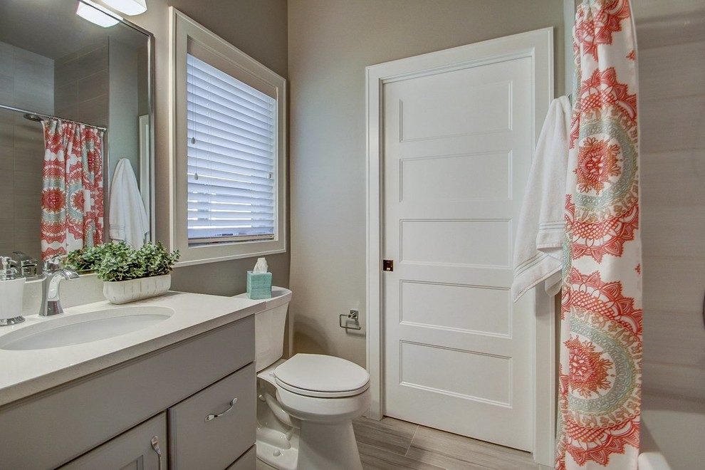 Photo of a mid-sized transitional 3/4 bathroom in Other with recessed-panel cabinets, an alcove tub, a shower/bathtub combo, grey walls, an undermount sink, a shower curtain, a two-piece toilet, porcelain floors, grey cabinets and solid surface benchtops.