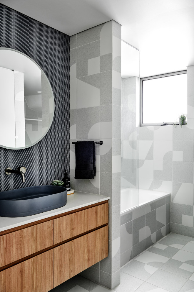 Inspiration for a mid-sized scandinavian bathroom in Sydney with medium wood cabinets, a drop-in tub, a shower/bathtub combo, blue tile, porcelain tile, porcelain floors, a vessel sink, engineered quartz benchtops and grey floor.