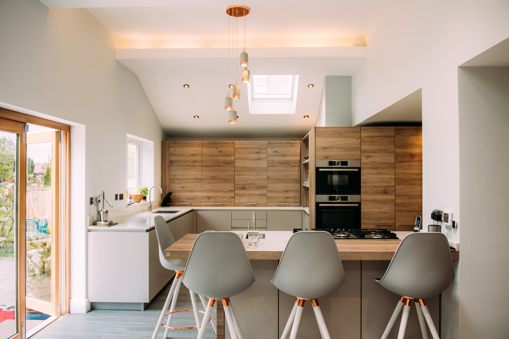 Inspiration for a mid-sized contemporary l-shaped open plan kitchen in Cheshire with black appliances, with island, an undermount sink, flat-panel cabinets, grey cabinets, grey floor and grey benchtop.