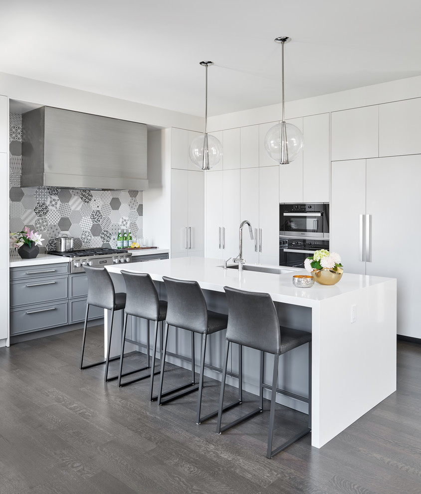 Photo of a mid-sized contemporary l-shaped open plan kitchen in Toronto with an undermount sink, flat-panel cabinets, white cabinets, quartz benchtops, multi-coloured splashback, porcelain splashback, stainless steel appliances, dark hardwood floors, with island and grey floor.