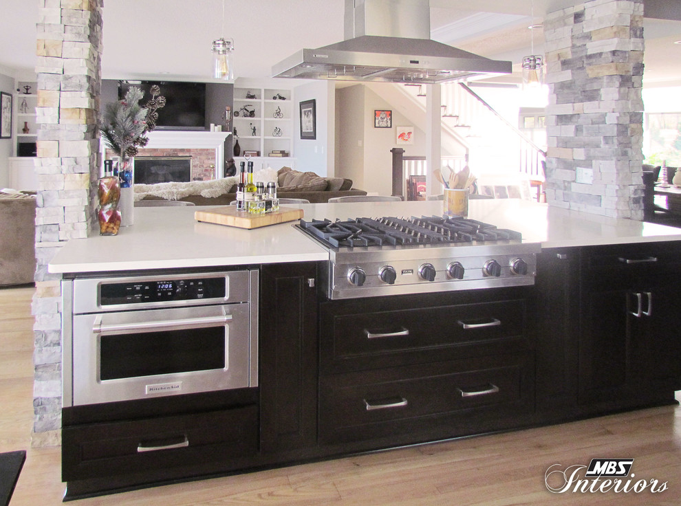 Large transitional l-shaped light wood floor eat-in kitchen photo with an undermount sink, recessed-panel cabinets, dark wood cabinets, quartz countertops, stainless steel appliances and an island