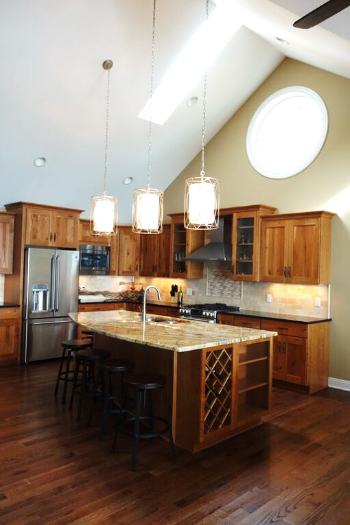 Inspiration for a rustic l-shaped dark wood floor eat-in kitchen remodel with an undermount sink, recessed-panel cabinets, medium tone wood cabinets, granite countertops, beige backsplash, stone tile backsplash, stainless steel appliances and an island