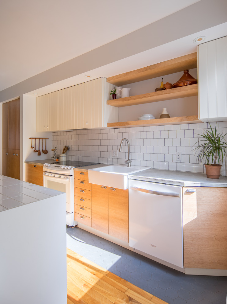 This is an example of a mid-sized contemporary galley eat-in kitchen in Montreal with a single-bowl sink, flat-panel cabinets, medium wood cabinets, tile benchtops, white splashback, ceramic splashback, white appliances, ceramic floors, with island and grey floor.