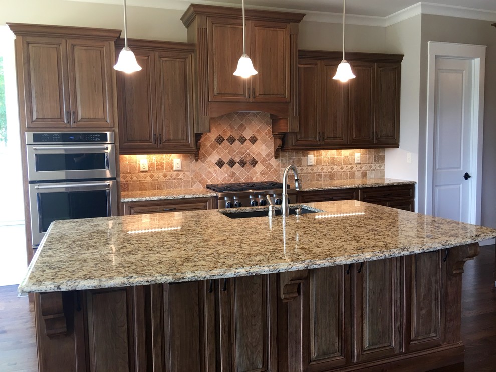 Inspiration for a large transitional l-shaped kitchen in Atlanta with an undermount sink, raised-panel cabinets, medium wood cabinets, granite benchtops, beige splashback, mosaic tile splashback, stainless steel appliances, dark hardwood floors and with island.