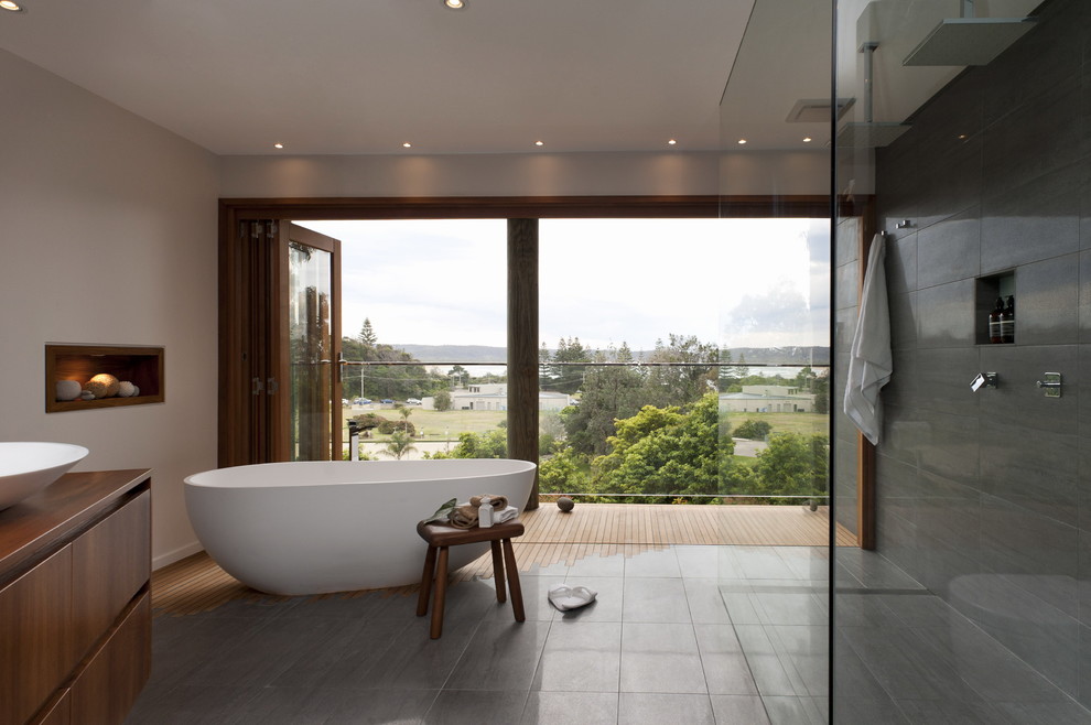 Design ideas for a contemporary master bathroom in Sydney with a vessel sink, furniture-like cabinets, medium wood cabinets, a freestanding tub, gray tile, white walls and ceramic floors.