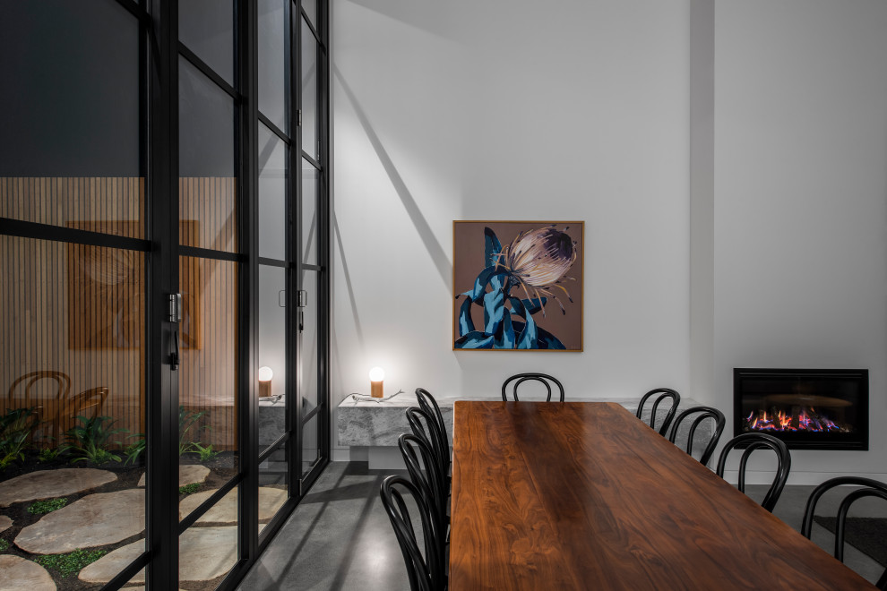 Idée de décoration pour une salle à manger ouverte sur le salon design de taille moyenne avec un mur blanc, sol en béton ciré, aucune cheminée, un manteau de cheminée en métal et un sol gris.