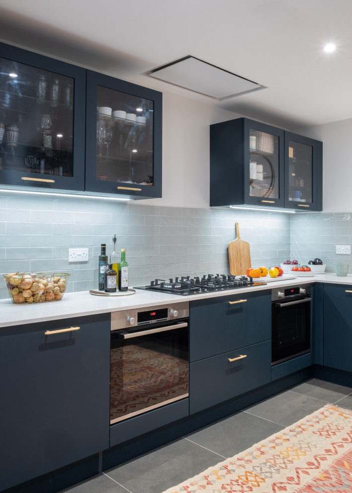 Bild på ett mellanstort eklektiskt vit vitt kök, med en enkel diskho, släta luckor, blå skåp, grönt stänkskydd, stänkskydd i porslinskakel, svarta vitvaror, skiffergolv och grönt golv