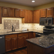 Small mountain style u-shaped medium tone wood floor and brown floor enclosed kitchen photo with an undermount sink, raised-panel cabinets, light wood cabinets, granite countertops, beige backsplash, stainless steel appliances and a peninsula