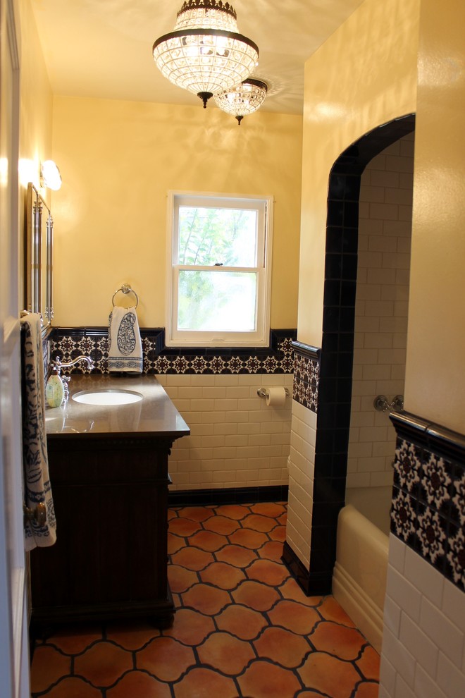 This is an example of a mid-sized mediterranean bathroom in Orange County with furniture-like cabinets, medium wood cabinets, an alcove tub, an alcove shower, a two-piece toilet, multi-coloured tile, ceramic tile, white walls, terra-cotta floors, an undermount sink and engineered quartz benchtops.