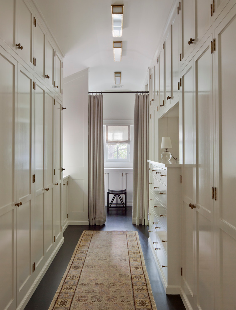 Idées déco pour un dressing room classique neutre avec un placard à porte shaker, des portes de placard blanches, parquet foncé et un sol marron.