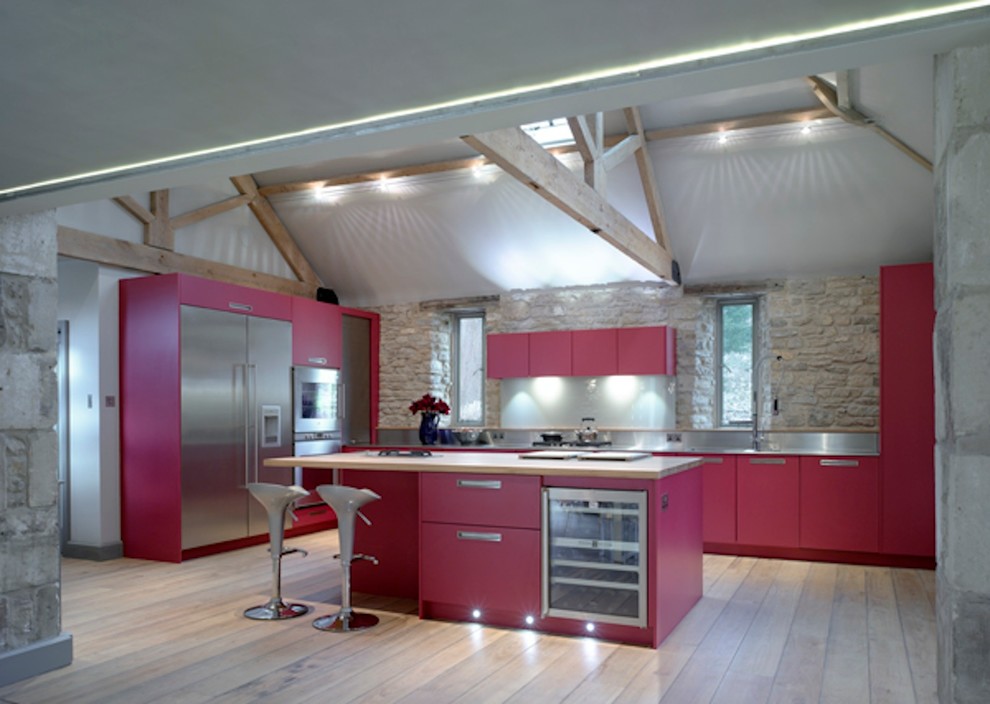 Large contemporary open plan kitchen in London with a submerged sink, flat-panel cabinets, red cabinets, stainless steel worktops, metallic splashback, stainless steel appliances and an island.