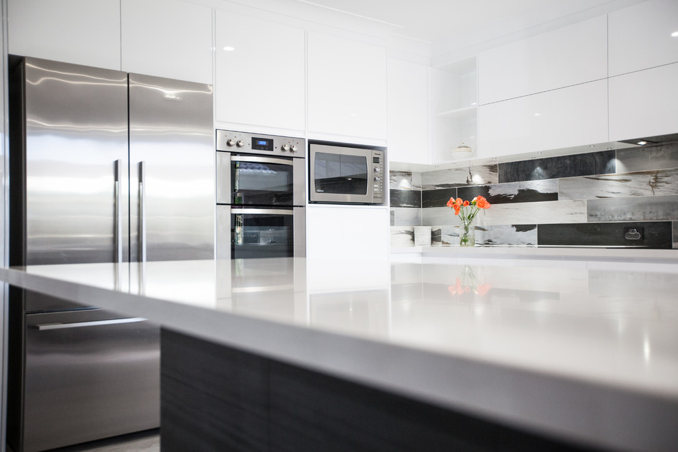 Mid-sized contemporary u-shaped eat-in kitchen in Sunshine Coast with a drop-in sink, white cabinets, quartz benchtops, grey splashback, stone tile splashback, stainless steel appliances, cement tiles, a peninsula, grey floor and white benchtop.