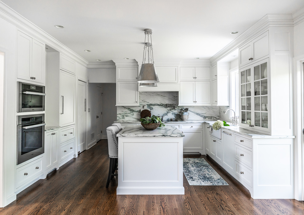 This is an example of a mid-sized transitional u-shaped eat-in kitchen in Philadelphia with a farmhouse sink, flat-panel cabinets, white cabinets, marble benchtops, marble splashback, panelled appliances, dark hardwood floors and with island.