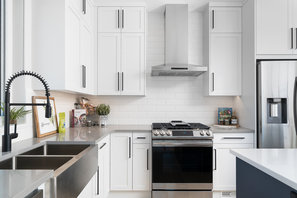 Medium sized classic l-shaped kitchen/diner in Vancouver with a double-bowl sink, shaker cabinets, white cabinets, engineered stone countertops, white splashback, metro tiled splashback, stainless steel appliances, light hardwood flooring, an island, brown floors and white worktops.