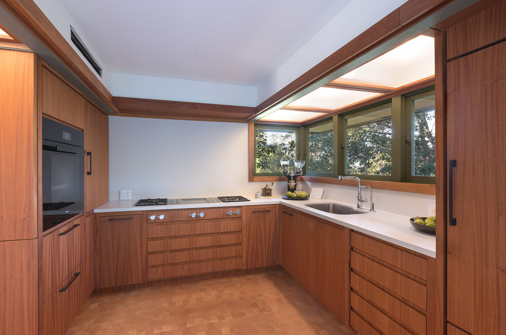 Inspiration for a small midcentury u-shaped separate kitchen in Los Angeles with an undermount sink, flat-panel cabinets, medium wood cabinets, solid surface benchtops, white splashback, panelled appliances, medium hardwood floors, no island, white benchtop and brown floor.