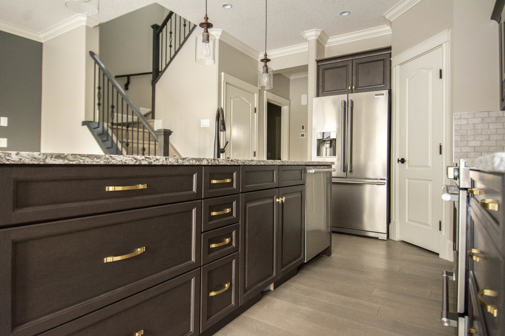 Example of a mid-sized transitional l-shaped medium tone wood floor and brown floor open concept kitchen design in Calgary with an undermount sink, raised-panel cabinets, dark wood cabinets, granite countertops, gray backsplash, porcelain backsplash, stainless steel appliances and an island
