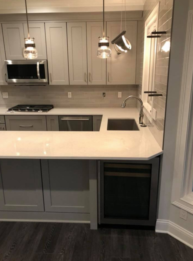 Transitional u-shaped gray floor kitchen photo with an undermount sink, recessed-panel cabinets, gray cabinets, gray backsplash, stainless steel appliances and white countertops