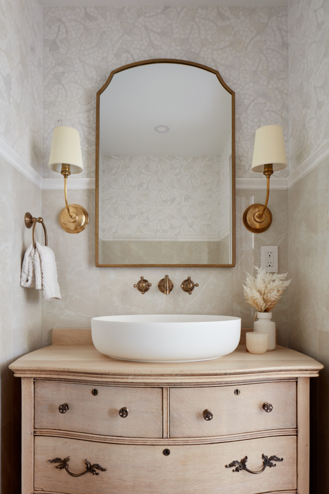 Foto på ett medelhavsstil beige toalett, med släta luckor, skåp i ljust trä, beige kakel, beige väggar, ett fristående handfat och träbänkskiva
