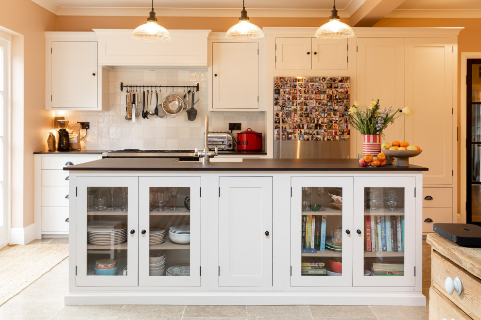 Example of a classic galley gray floor kitchen design in Other with an island, a farmhouse sink, shaker cabinets, white cabinets, white backsplash, stainless steel appliances and black countertops