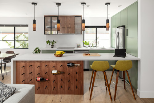 Modern kitchen with sage-green RTA cabinets, white quartz peninsula, walnut wine-peg island, pendant lights, and mid-century stools.