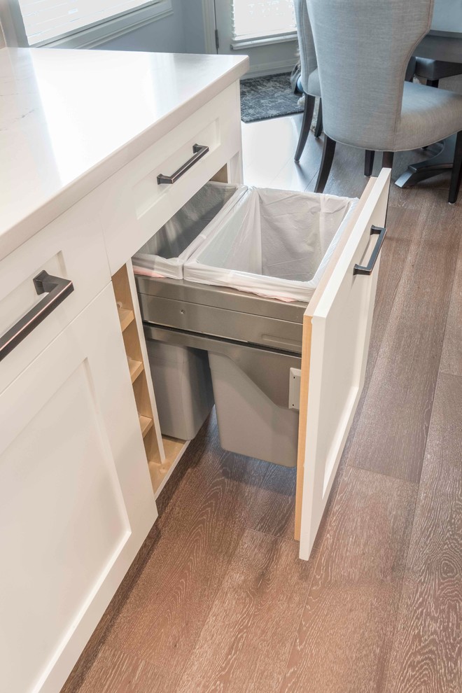 Example of a mid-sized transitional u-shaped medium tone wood floor and brown floor home design design in Calgary with an undermount sink, flat-panel cabinets, white cabinets, marble countertops, gray backsplash, ceramic backsplash, paneled appliances and an island