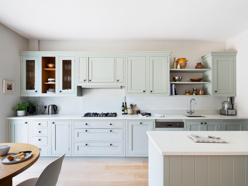 This is an example of a transitional galley kitchen in London with an undermount sink, shaker cabinets, grey cabinets, panelled appliances, light hardwood floors, with island, beige floor and white benchtop.