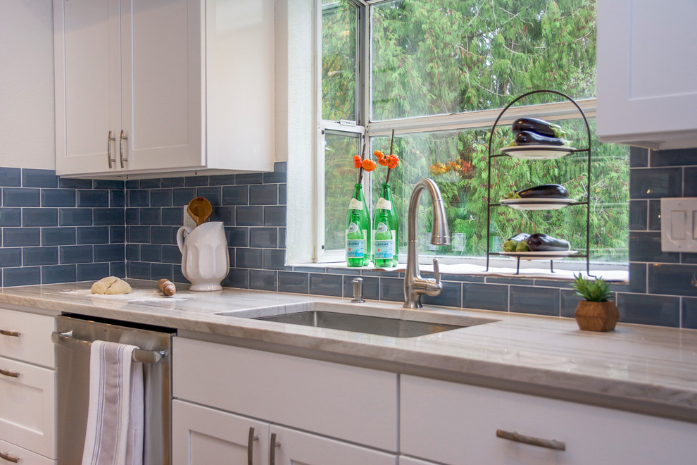 Example of a large transitional galley medium tone wood floor and brown floor open concept kitchen design in Seattle with an undermount sink, shaker cabinets, white cabinets, quartz countertops, blue backsplash, subway tile backsplash, stainless steel appliances, an island and multicolored countertops