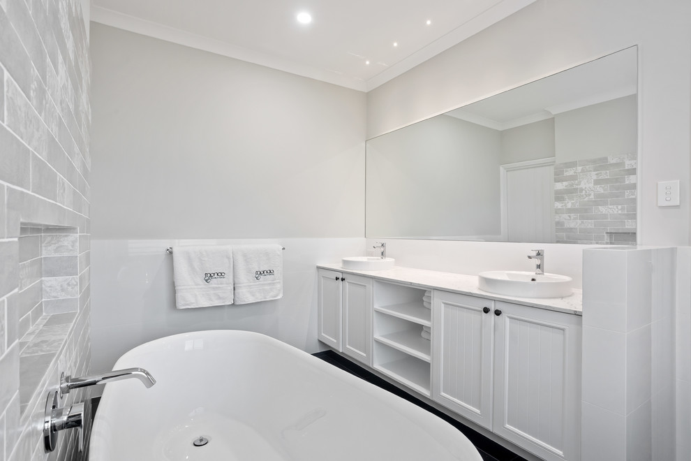 Inspiration for a mid-sized beach style master bathroom in Perth with shaker cabinets, white cabinets, a freestanding tub, an open shower, white tile, porcelain tile, white walls, porcelain floors, a drop-in sink, marble benchtops, grey floor, an open shower and white benchtops.
