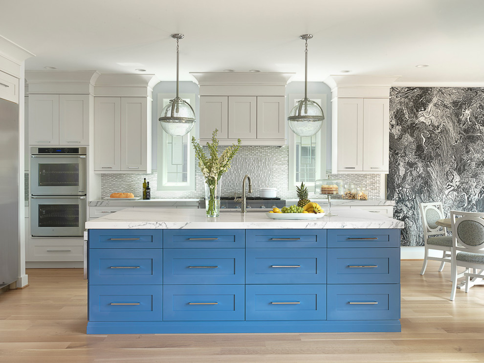 Design ideas for a large transitional eat-in kitchen in St Louis with an undermount sink, shaker cabinets, blue cabinets, solid surface benchtops, glass tile splashback, stainless steel appliances, light hardwood floors, with island and grey splashback.