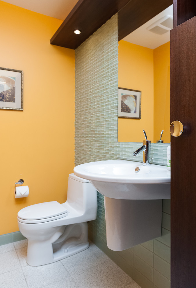 This is an example of a midcentury bathroom in Portland with white cabinets, a one-piece toilet, green tile, glass tile, orange walls, porcelain floors, a wall-mount sink, a single vanity and a floating vanity.