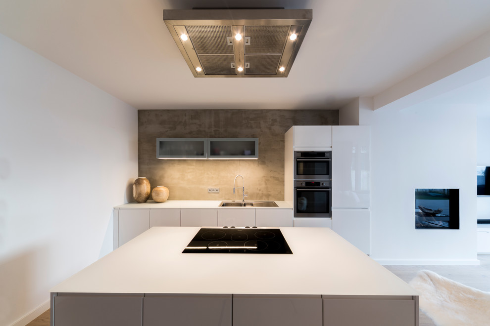 Photo of a large contemporary open plan kitchen in Berlin with a drop-in sink, flat-panel cabinets, white cabinets, black appliances, light hardwood floors and with island.