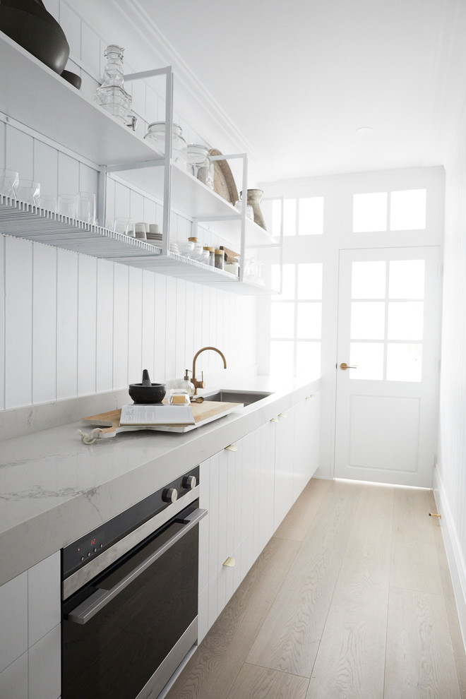 Large beach style single-wall kitchen in Sydney with white cabinets, white splashback, no island, white benchtop, an undermount sink, light hardwood floors and beige floor.