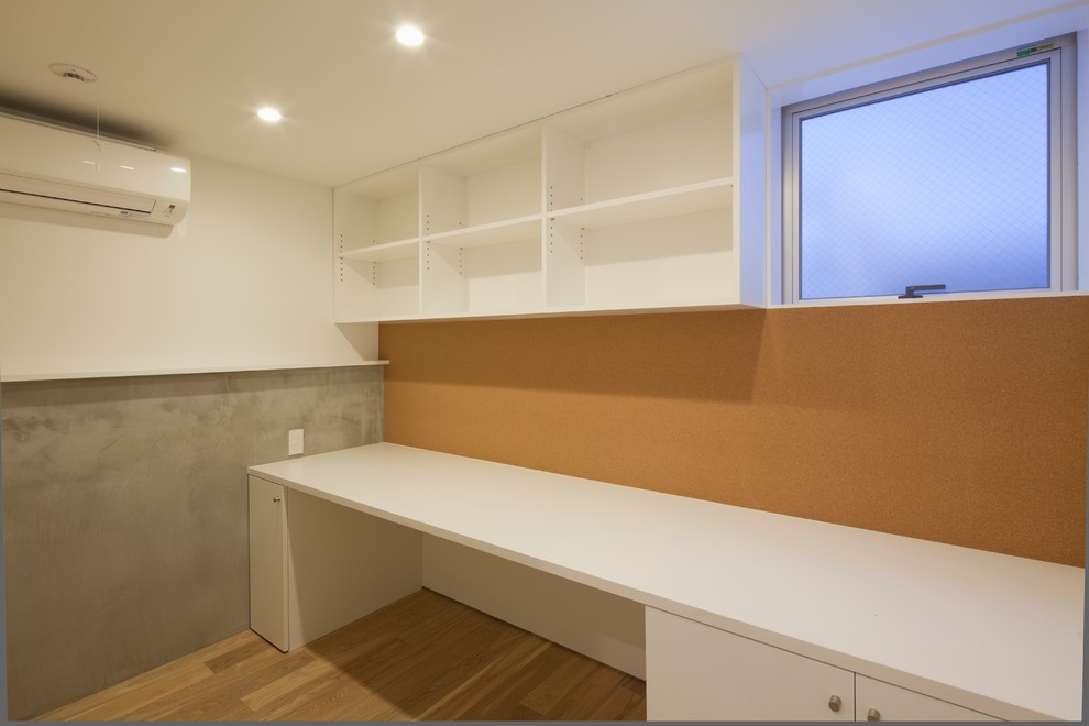 This is an example of a modern home studio in Tokyo with brown walls, plywood floors, no fireplace, a built-in desk and beige floor.