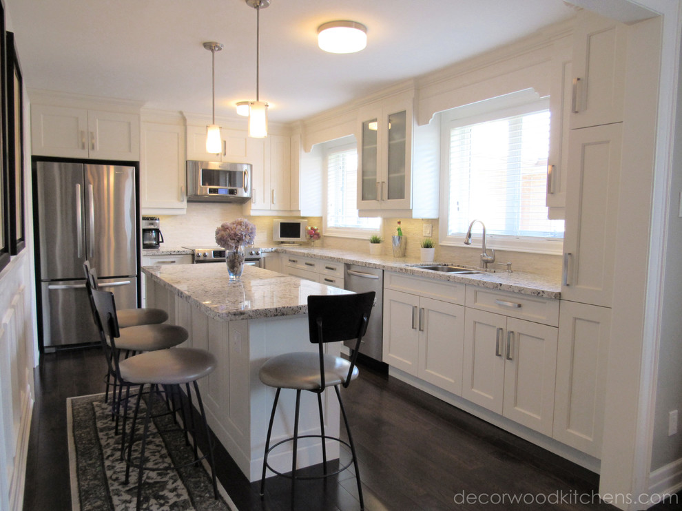 Example of a mid-sized transitional l-shaped dark wood floor enclosed kitchen design in Toronto with an undermount sink, flat-panel cabinets, white cabinets, granite countertops, white backsplash, stone tile backsplash, stainless steel appliances and an island