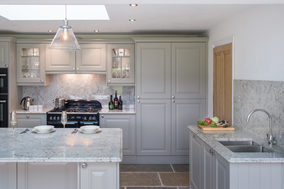 Mid-sized country u-shaped open plan kitchen in Cornwall with a drop-in sink, shaker cabinets, grey cabinets, granite benchtops, multi-coloured splashback, black appliances, slate floors, with island, beige floor and multi-coloured benchtop.