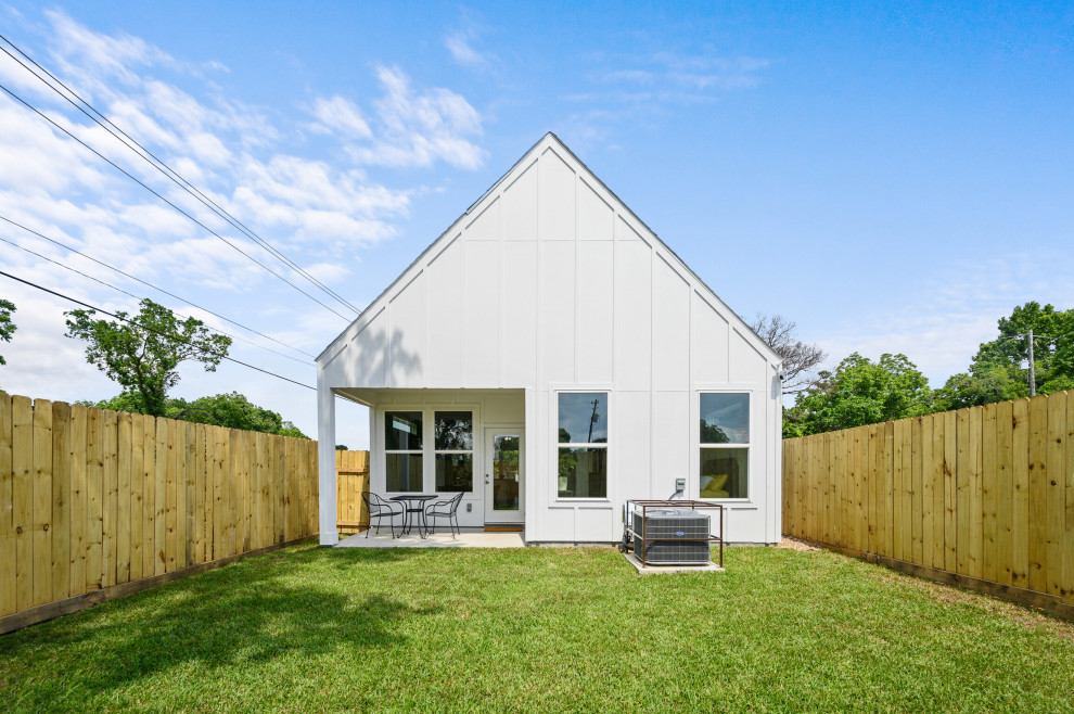 Design ideas for a mid-sized modern one-storey yellow house exterior in Houston with concrete fiberboard siding, a gable roof, a shingle roof, a black roof and board and batten siding.