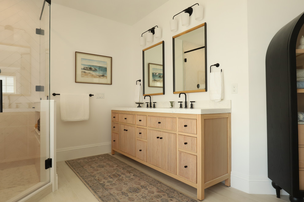 Photo of a large coastal ensuite bathroom in Portland Maine with freestanding cabinets, light wood cabinets, a freestanding bath, a double shower, white walls, wood-effect flooring, a submerged sink, engineered stone worktops, beige floors, a hinged door, white worktops, double sinks and a freestanding vanity unit.