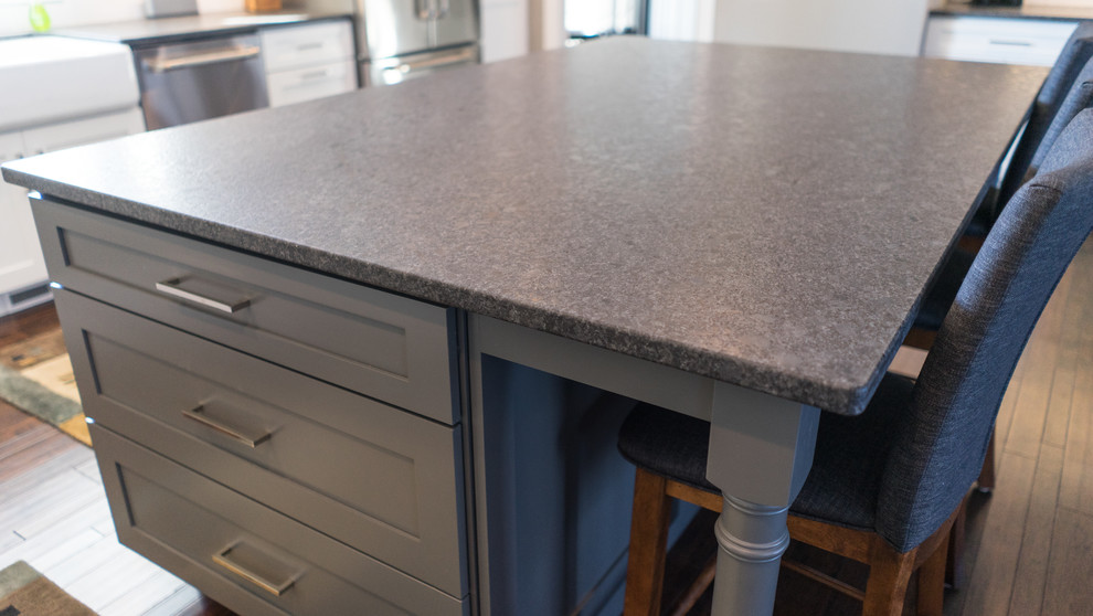 Example of a large transitional u-shaped eat-in kitchen design with a farmhouse sink, flat-panel cabinets, white cabinets, granite countertops, white backsplash, ceramic backsplash, stainless steel appliances and an island