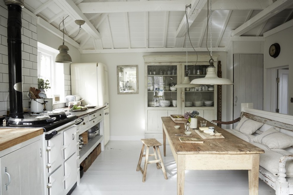 Mid-sized country single-wall eat-in kitchen in Cornwall with shaker cabinets, white cabinets, wood benchtops, white splashback, ceramic splashback, white appliances, painted wood floors and white floor.