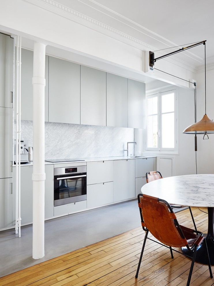 Photo of a mid-sized scandinavian single-wall open plan kitchen in Paris with flat-panel cabinets, grey cabinets, grey splashback, stone slab splashback, panelled appliances, an undermount sink, marble benchtops, concrete floors and no island.