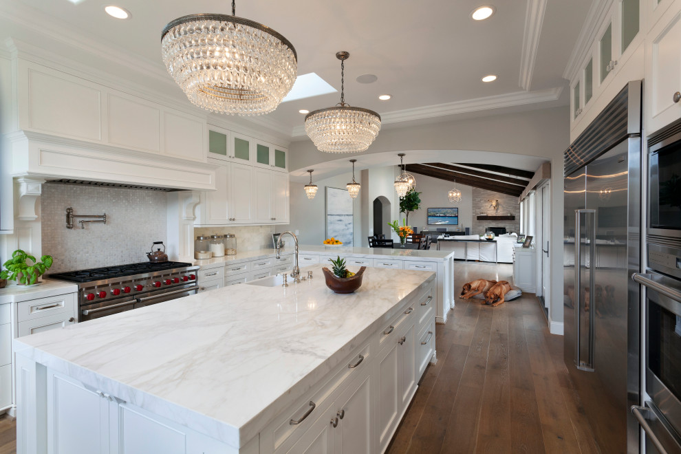 Inspiration for an expansive traditional u-shaped kitchen/diner in Santa Barbara with a submerged sink, raised-panel cabinets, white cabinets, marble worktops, white splashback, marble splashback, stainless steel appliances, medium hardwood flooring, an island, brown floors, white worktops and a coffered ceiling.