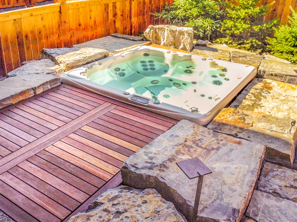 This is an example of a mid-sized traditional backyard custom-shaped pool in Calgary with a hot tub and natural stone pavers.