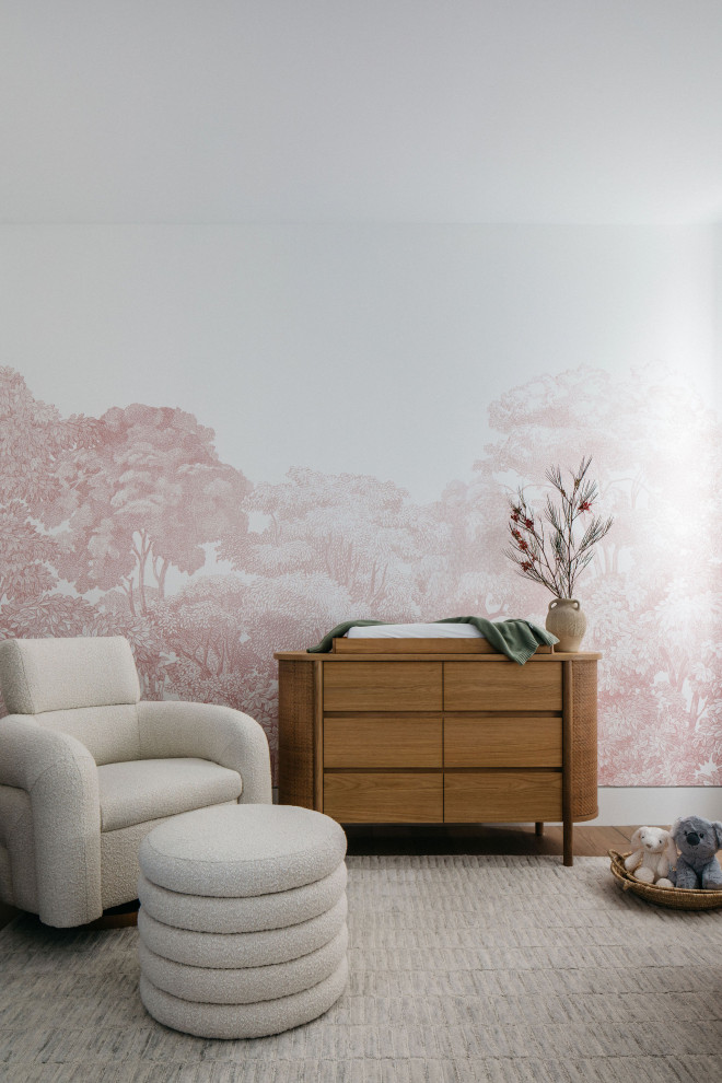 Ejemplo de habitación de bebé actual con paredes rosas, suelo de madera en tonos medios, suelo marrón y papel pintado
