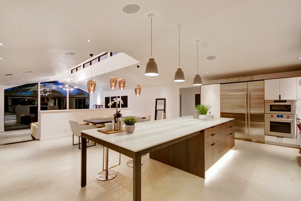 Photo of a country l-shaped eat-in kitchen in San Francisco with flat-panel cabinets, white cabinets, marble benchtops, stainless steel appliances, concrete floors, with island, grey floor and white benchtop.